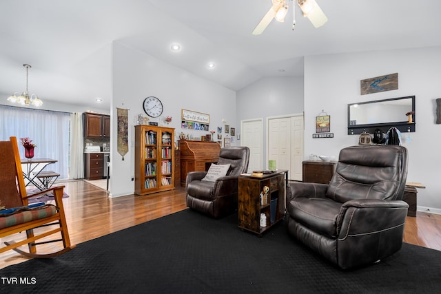 living room with ceiling fan with notable chandelier, high vaulted ceiling, and light hardwood / wood-style floors