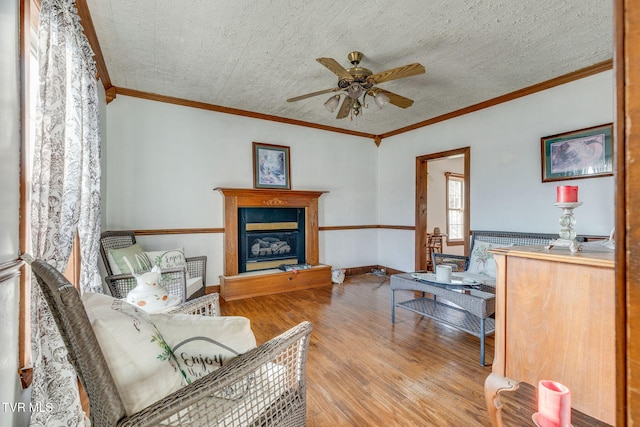 living room featuring ceiling fan, ornamental molding, a textured ceiling, and light wood-type flooring