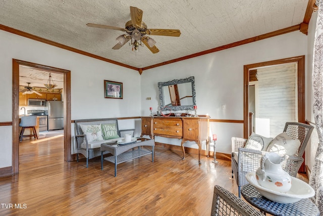 sitting room featuring ceiling fan, ornamental molding, light hardwood / wood-style floors, and a textured ceiling