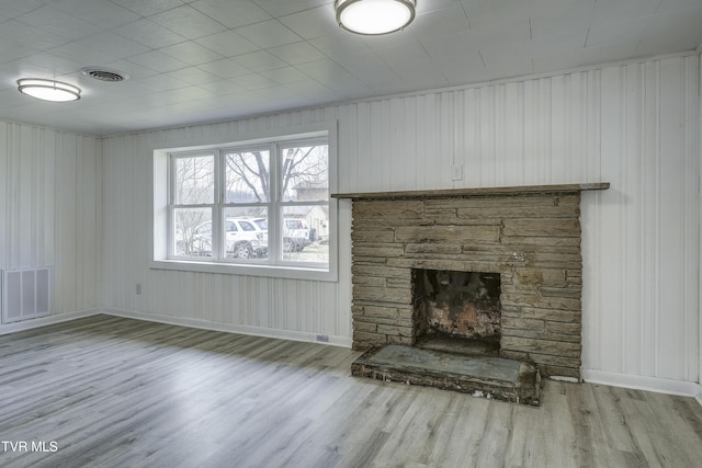 unfurnished living room featuring a stone fireplace and light wood-type flooring