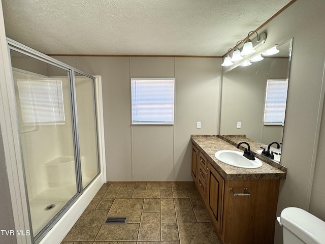 bathroom with vanity, ornamental molding, a textured ceiling, a shower with shower door, and toilet