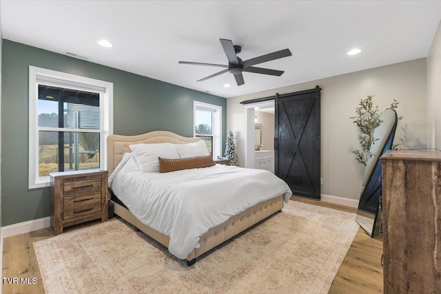 bedroom featuring a barn door, connected bathroom, ceiling fan, and light hardwood / wood-style flooring