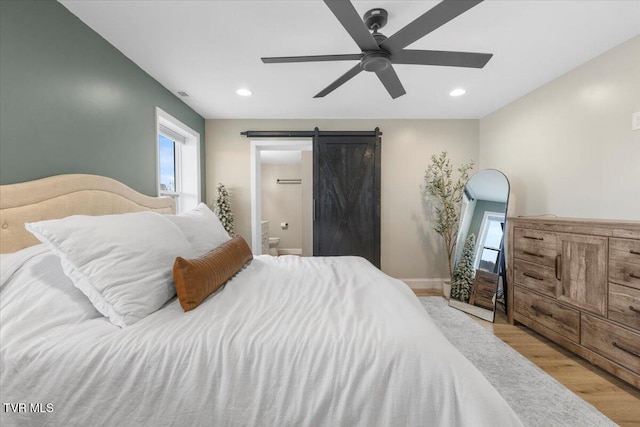 bedroom with ceiling fan, connected bathroom, a barn door, and light hardwood / wood-style floors