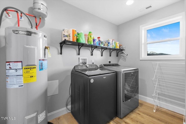 clothes washing area with water heater, separate washer and dryer, and light hardwood / wood-style flooring