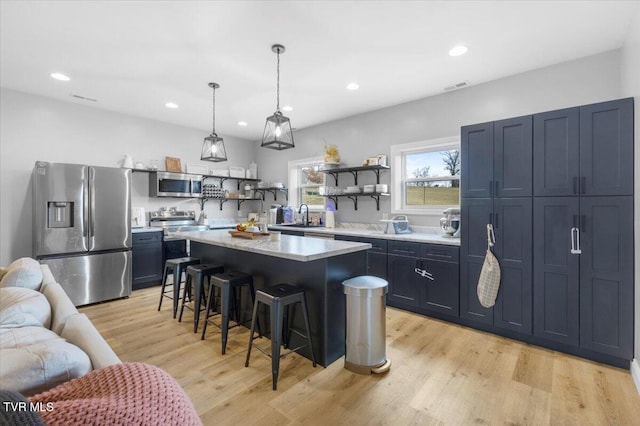 kitchen with pendant lighting, a breakfast bar area, appliances with stainless steel finishes, a center island, and light hardwood / wood-style floors