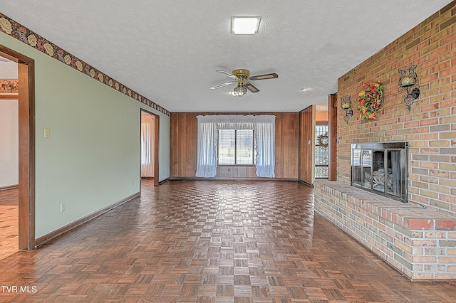 unfurnished living room featuring a brick fireplace, dark parquet floors, a textured ceiling, and wood walls