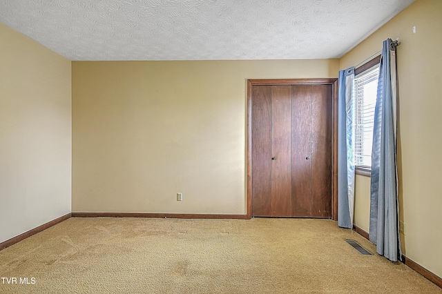 unfurnished bedroom featuring light colored carpet, a closet, and a textured ceiling