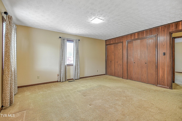 unfurnished bedroom featuring multiple closets, light carpet, a textured ceiling, and wood walls