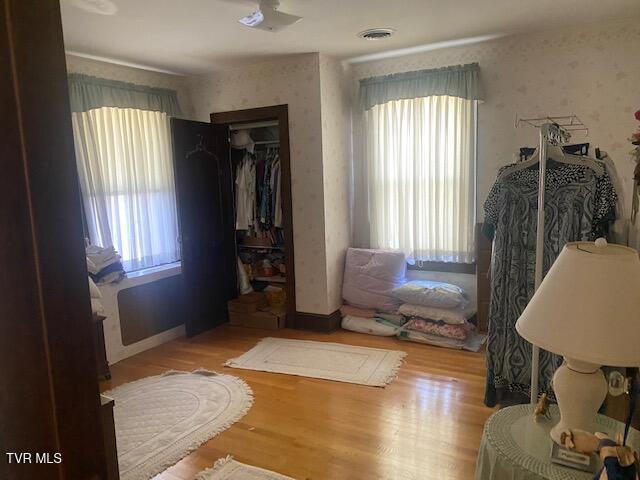 bedroom featuring wallpapered walls, wood finished floors, visible vents, and a closet