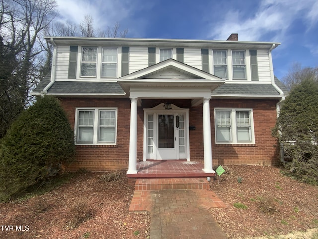 traditional-style home featuring brick siding, a porch, and a shingled roof