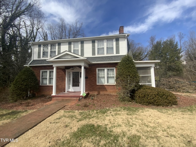 traditional home with a shingled roof, a front lawn, brick siding, and a chimney