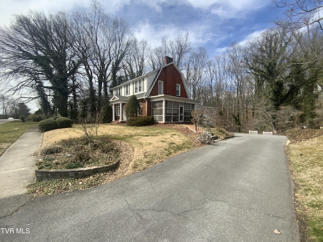 view of side of home with a gambrel roof, aphalt driveway, a yard, a sunroom, and a chimney