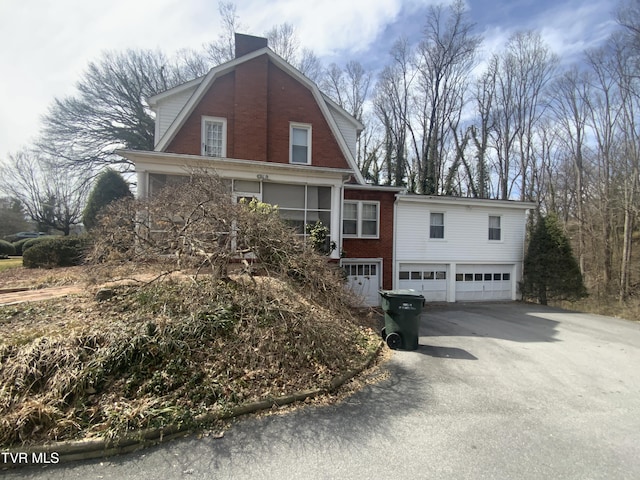 colonial inspired home with driveway, brick siding, a garage, and a gambrel roof