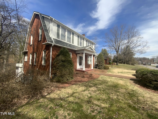 view of home's exterior featuring roof with shingles, a yard, a gambrel roof, a chimney, and brick siding