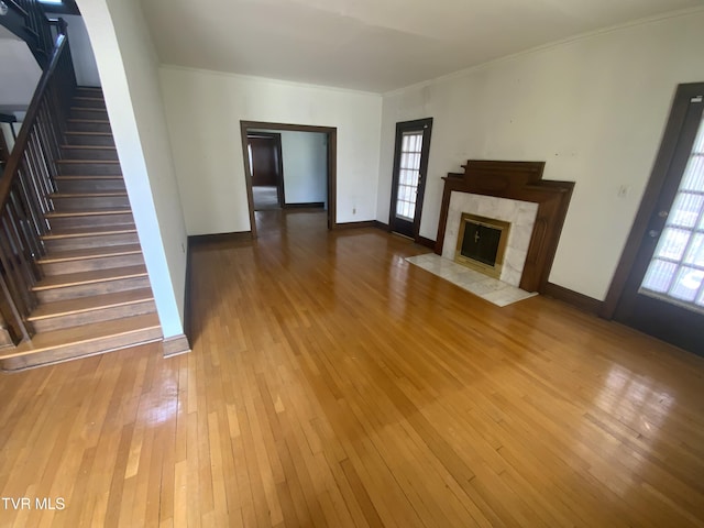 unfurnished living room featuring stairway, a fireplace, light wood-type flooring, and crown molding