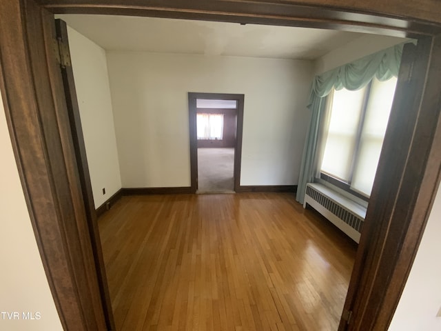 unfurnished room with baseboards, wood-type flooring, and radiator heating unit