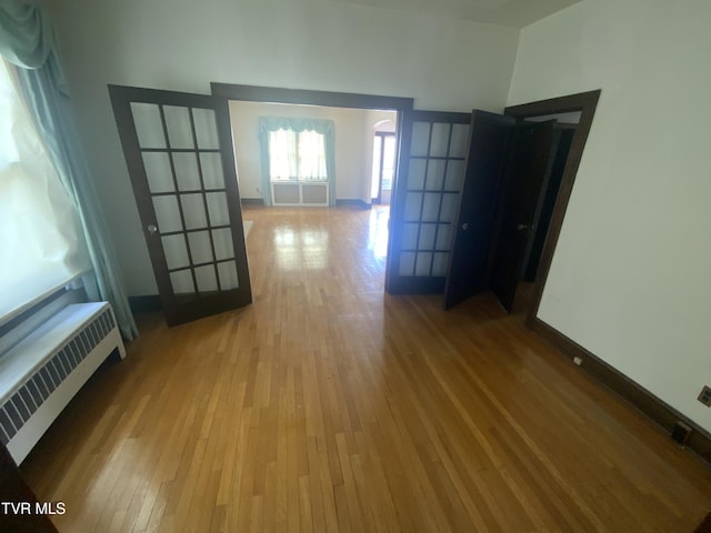 hall with french doors, baseboards, hardwood / wood-style floors, and radiator heating unit