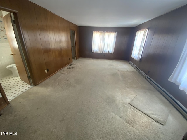 interior space with light carpet, wood walls, and a baseboard heating unit