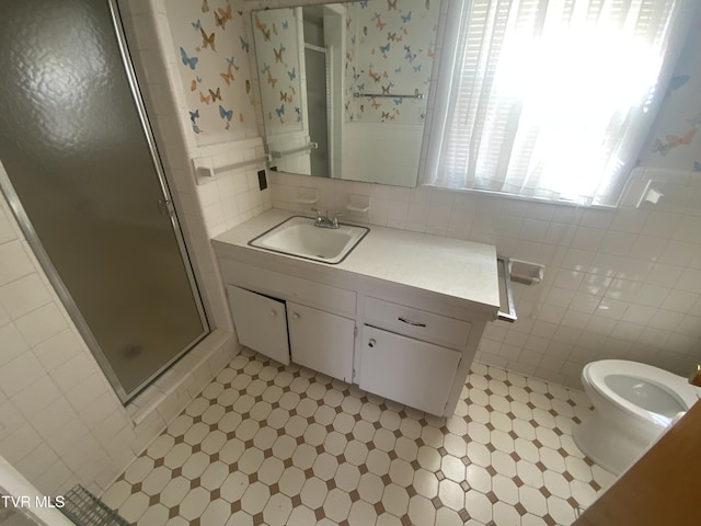 bathroom with a shower stall, wallpapered walls, toilet, vanity, and tile walls