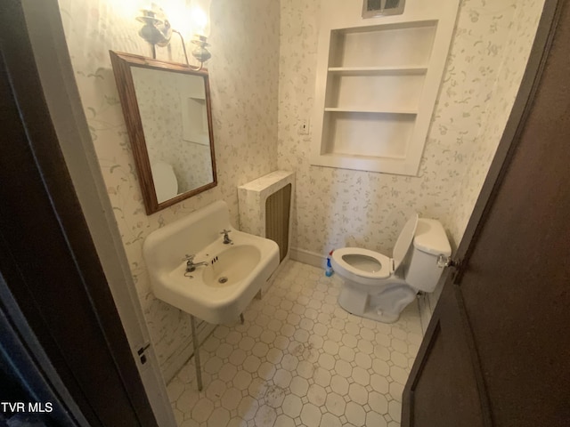 half bathroom with built in features, toilet, wallpapered walls, and a sink