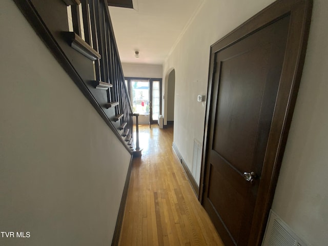 hallway featuring arched walkways, visible vents, light wood finished floors, and ornamental molding