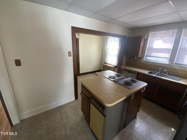 kitchen featuring a sink, a drop ceiling, a center island, light countertops, and baseboards