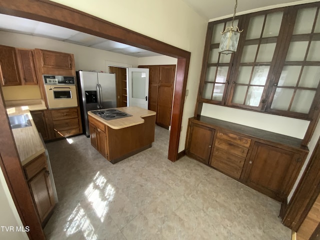 kitchen with brown cabinets, a sink, a kitchen island, stainless steel appliances, and light floors