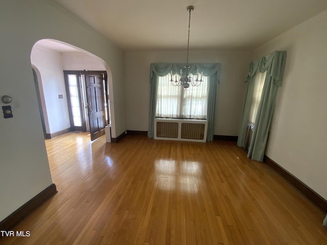 unfurnished dining area with baseboards, radiator heating unit, arched walkways, wood-type flooring, and a notable chandelier