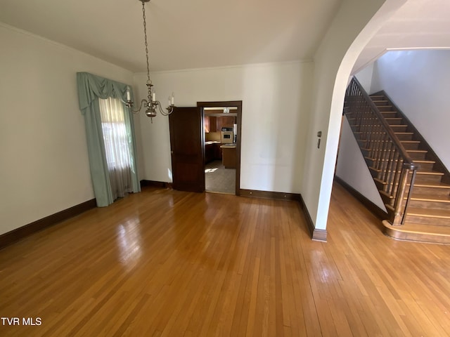 unfurnished room featuring crown molding, baseboards, stairway, hardwood / wood-style floors, and a notable chandelier