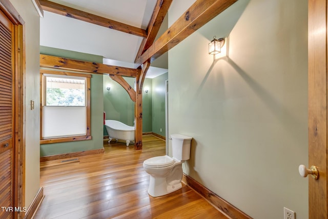 bathroom featuring wood-type flooring, a tub, vaulted ceiling with beams, and toilet