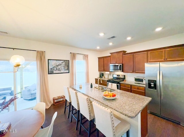 kitchen with sink, dark hardwood / wood-style floors, a kitchen breakfast bar, an island with sink, and stainless steel appliances