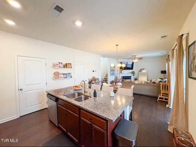 kitchen with dark wood-type flooring, sink, dishwasher, an island with sink, and light stone countertops