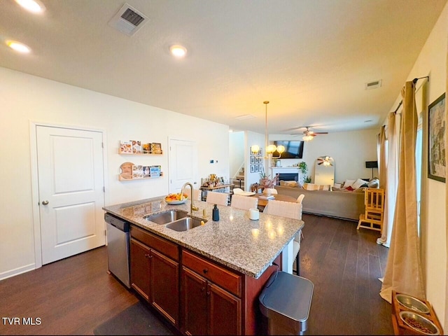 kitchen featuring dark wood-type flooring, sink, light stone counters, stainless steel dishwasher, and a kitchen island with sink