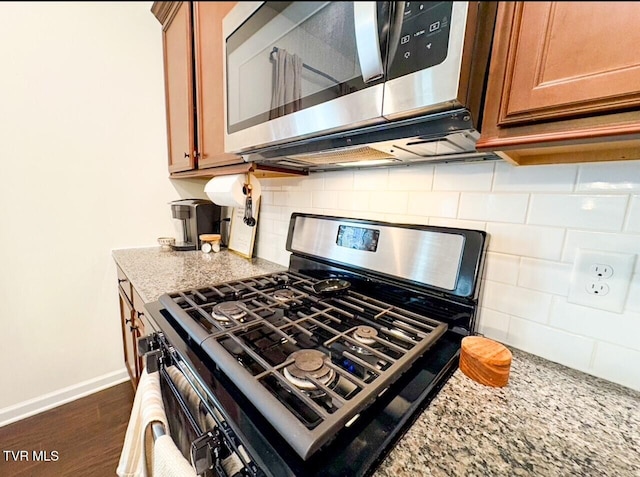 interior details with light stone countertops, appliances with stainless steel finishes, dark hardwood / wood-style flooring, and decorative backsplash