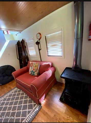 sitting room with wood ceiling, wood-type flooring, vaulted ceiling, and a wood stove