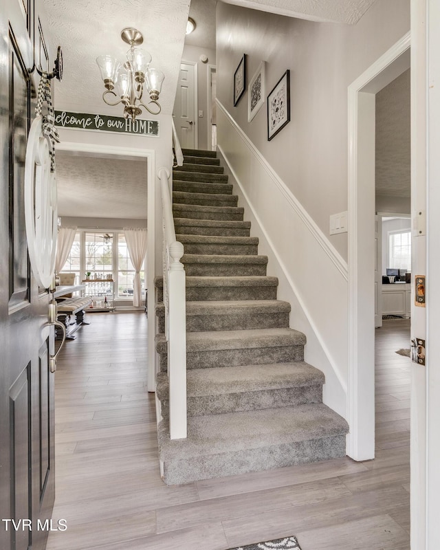 stairway with an inviting chandelier, plenty of natural light, and hardwood / wood-style floors