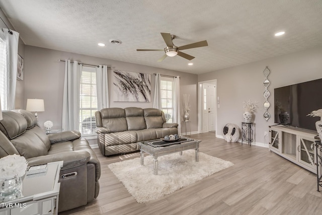 living room with ceiling fan, a textured ceiling, and light wood-type flooring