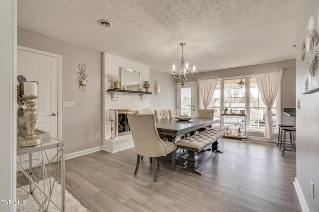 dining space with a brick fireplace, an inviting chandelier, a textured ceiling, and light hardwood / wood-style floors