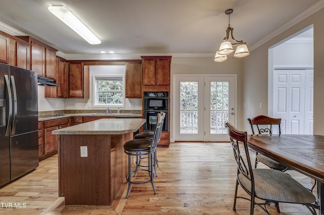 kitchen featuring sink, hanging light fixtures, black appliances, a kitchen island, and light wood-type flooring