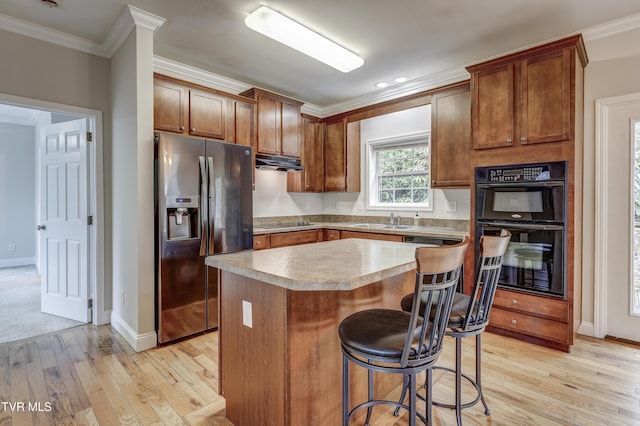 kitchen featuring sink, crown molding, a center island, black appliances, and light wood-type flooring