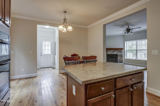 kitchen featuring pendant lighting, a fireplace, ornamental molding, a kitchen island, and light wood-type flooring