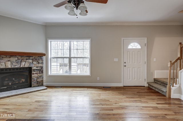 unfurnished living room with ceiling fan, ornamental molding, a stone fireplace, and light wood-type flooring