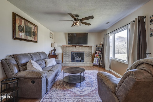 living room featuring a brick fireplace, a textured ceiling, ceiling fan, and light hardwood / wood-style flooring