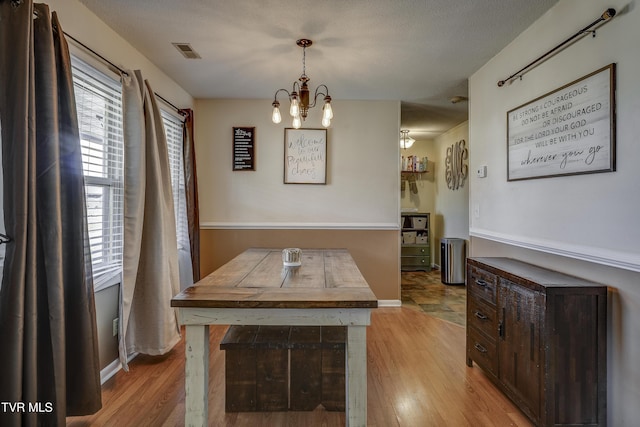 dining room with a textured ceiling, an inviting chandelier, and light hardwood / wood-style flooring