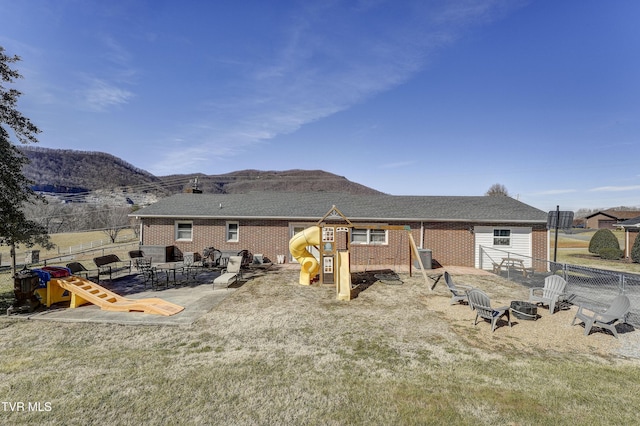 rear view of house with a mountain view, a lawn, a patio, and a playground