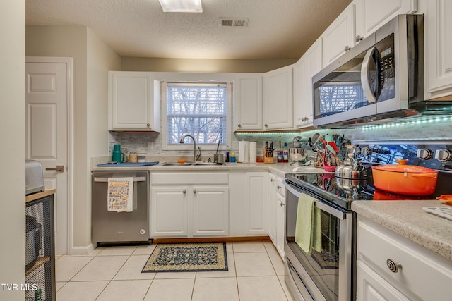 kitchen with appliances with stainless steel finishes, white cabinetry, sink, decorative backsplash, and light tile patterned floors