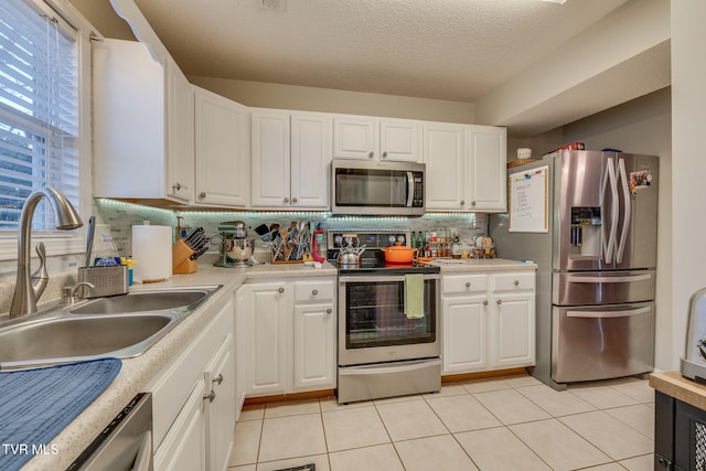 kitchen with white cabinetry, sink, decorative backsplash, light tile patterned floors, and stainless steel appliances