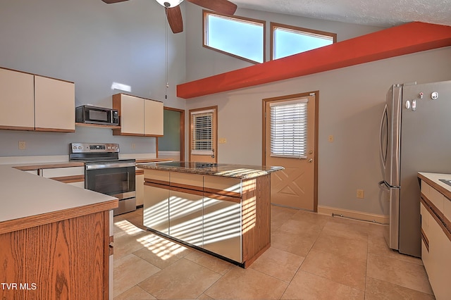 kitchen with light tile patterned floors, a kitchen island, ceiling fan, stainless steel appliances, and cream cabinetry