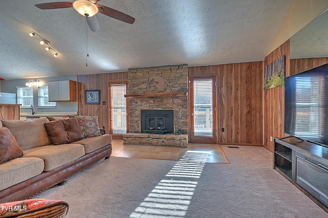 carpeted living room with ceiling fan, wooden walls, a textured ceiling, and a fireplace