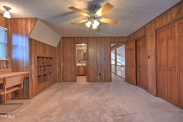 unfurnished bedroom featuring connected bathroom, wood walls, light colored carpet, multiple closets, and a textured ceiling